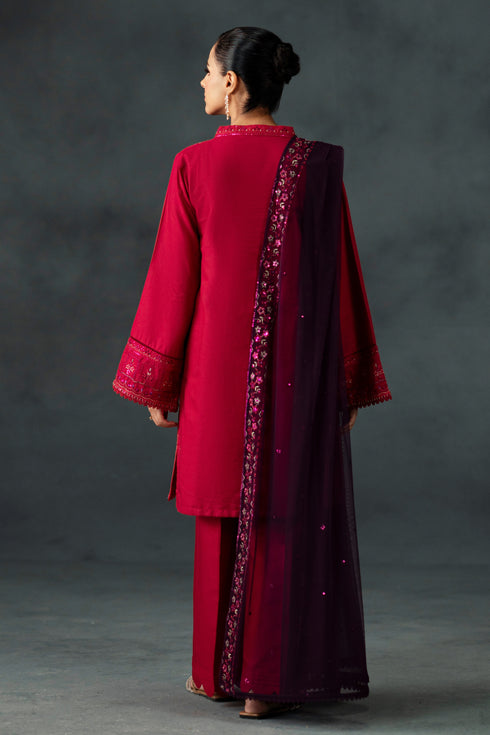 Woman wearing a red traditional outfit with intricate patterns on a gray background